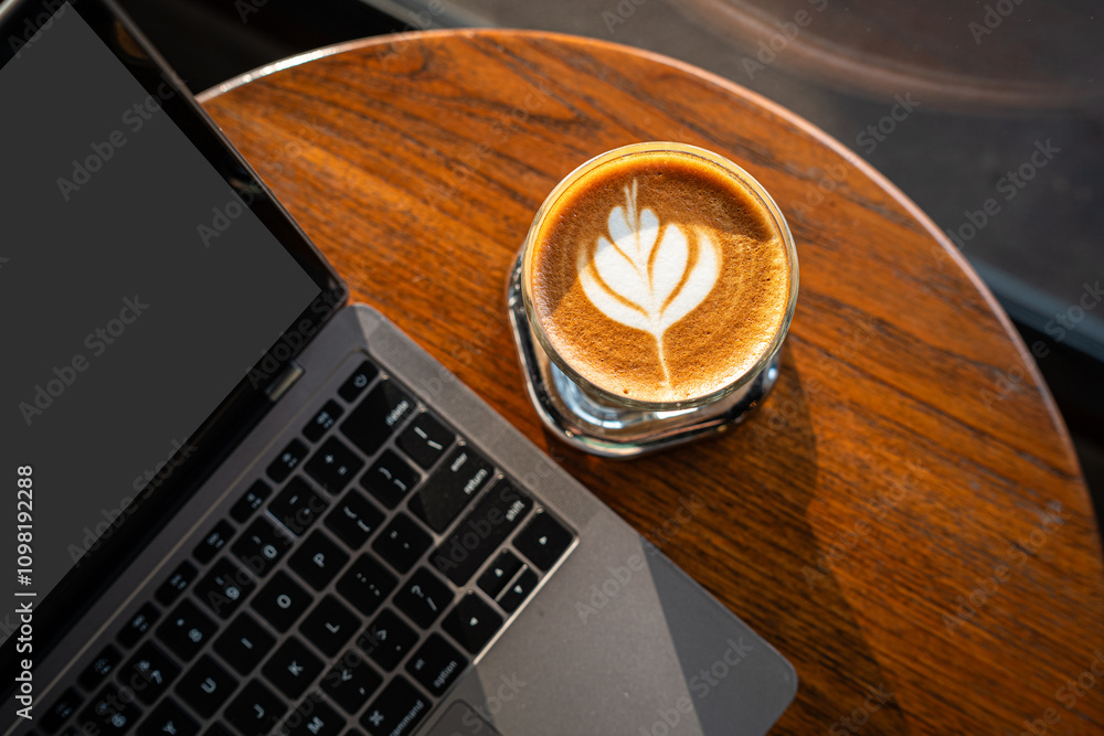 Close-up of Hot coffee latte with latte art milk foam in cup mug and laptop computer on wood desk office desk in coffee shop at the cafe,during business work concept