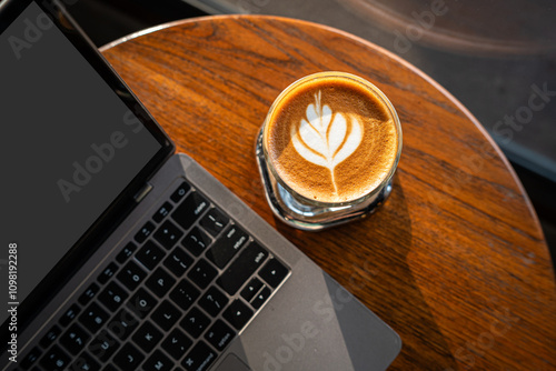 Obraz na płótnie Close-up of Hot coffee latte with latte art milk foam in cup mug and laptop computer on wood desk office desk in coffee shop at the cafe,during business work concept w salonie