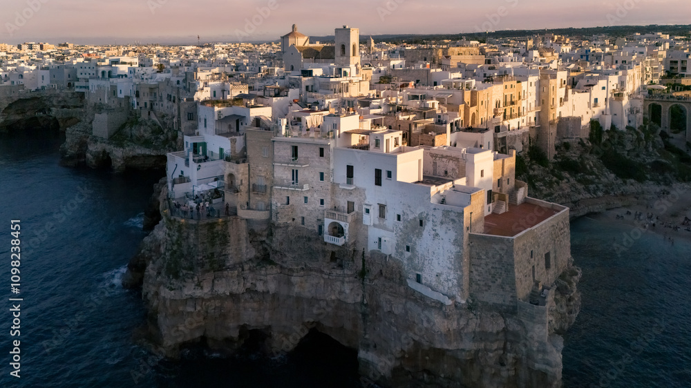Obraz premium Aerial view of white ancient mediterranean town on rocky seaside at sunset, Polignano a Mare, Italy
