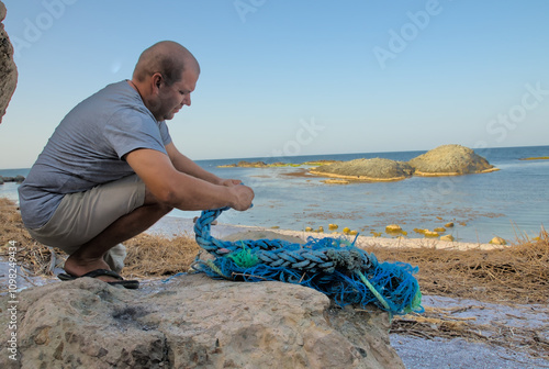 A person unbraiding a massive synthetic fishing rope on the shore of the sea