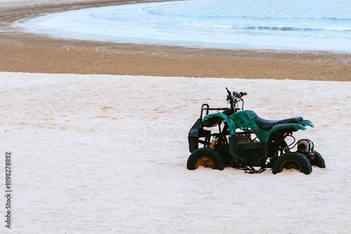 Old vintage green ATV on the sandy beach. Quad ATV all terrain vehicle parked on beach, Motor bikes ready for action with summer sun flaring on bright day. Outdoor extreme activity adrenaline sport. photo