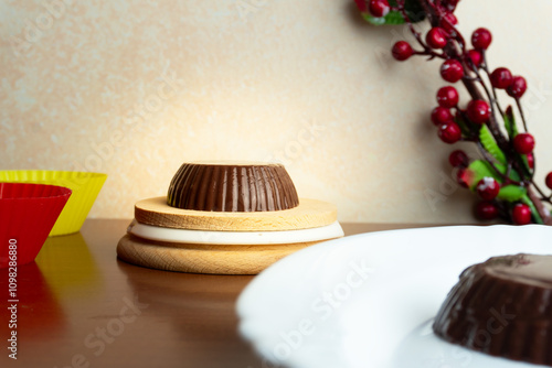 Vegan chocolate pudding placed on a wooden surface, next to two red and yellow cupcake stamps and a branch with some berries and leaves.  photo