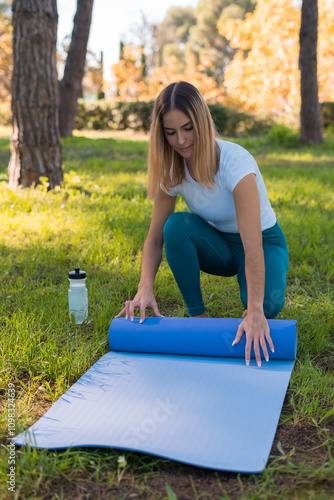 young woman spreading the mat on the ground in the park preparing to do yoga