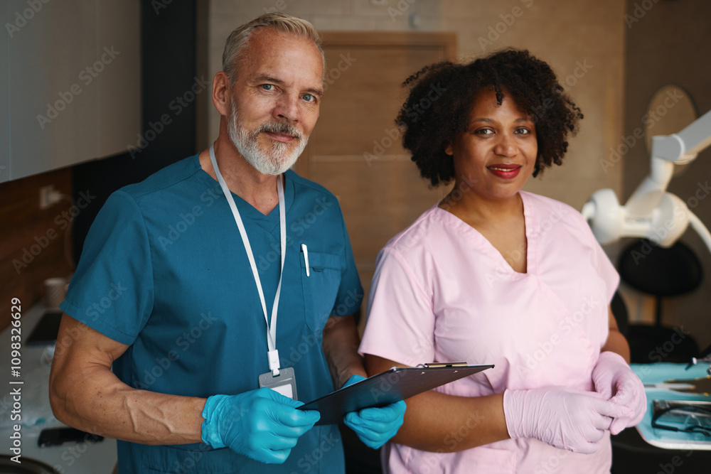 Obraz premium Portrait of smiling medical professionals standing together in an examination room holding a clipboard and wearing gloves demonstrating teamwork and professionalism
