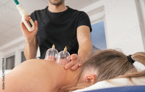 Therapist's hands performing vacuum cupping therapy treatment on female patient's skin. Image highlights relaxation and alternative medicine healthcare practices in traditional oriental clinic. photo