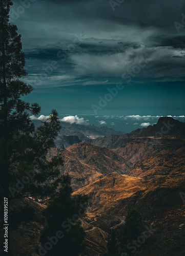 Dramatic mountain landscape under moody skies with rugged terrain and winding roads at sunset