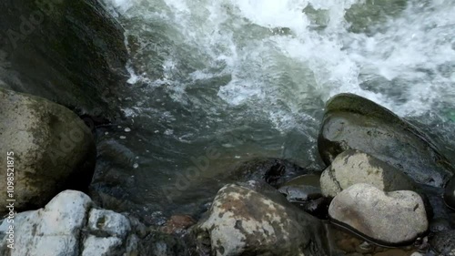 The flow of water hits the rocks on the river bank. Appearance of the river bank. The water looks rotating. Real time. Natural light photo