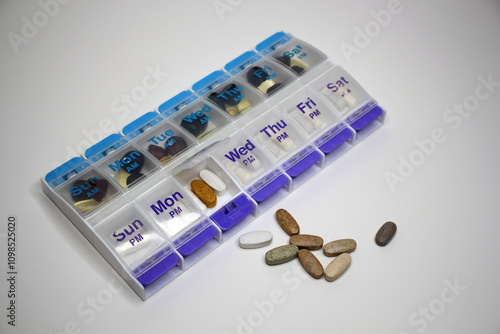 Weekly pill organizer with supplements and medications on white background.