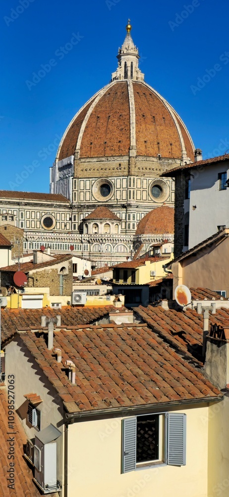 Fototapeta premium Florence, Italy - November 24, 2024: The iconic dome of Florence Cathedral, designed by Brunelleschi, rises above the historic terracotta rooftops under a vibrant blue sk