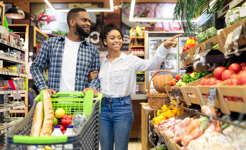 Black Family On Grocery Shopping In Supermarket. Happy African Couple Buying Organic Vegetabels And Fresh Fruits In Local Food Store Standing With Shop Cart. Customers Choosing Supplies photo