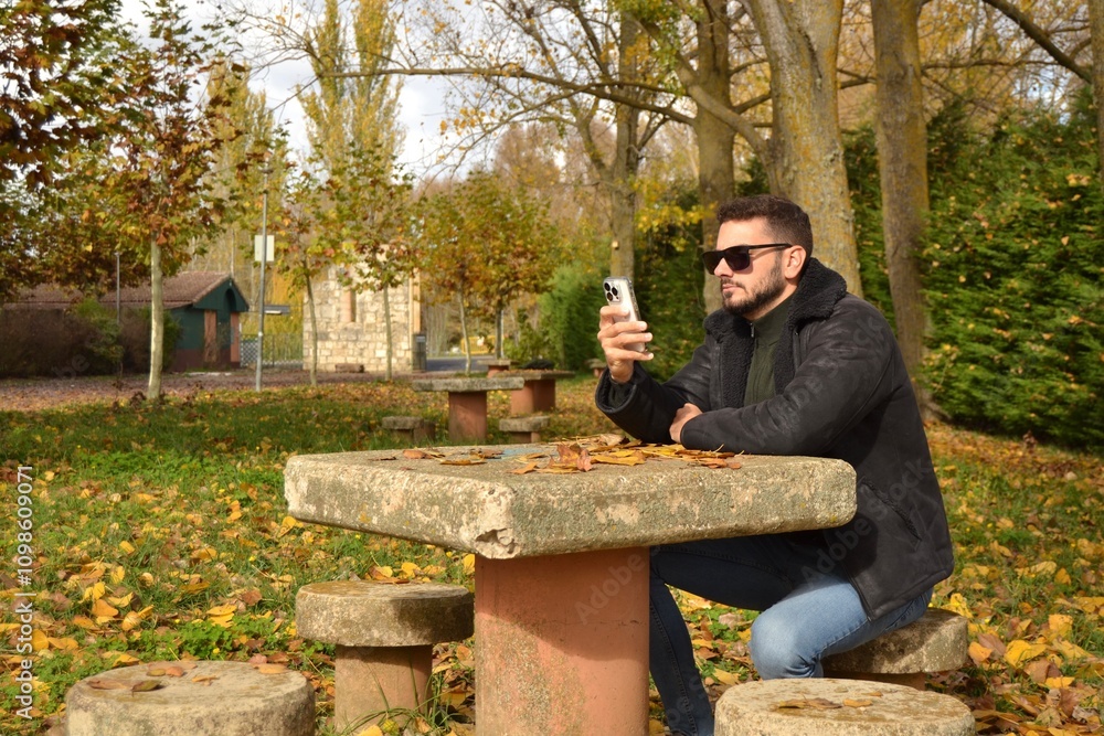 Fototapeta premium Young handsome guy walking through the park or forest enjoying the autumn. New technologies, mobile phone. Looking for coverage. Taking advantage of free time to read. E-book.Reconnecting with oneself