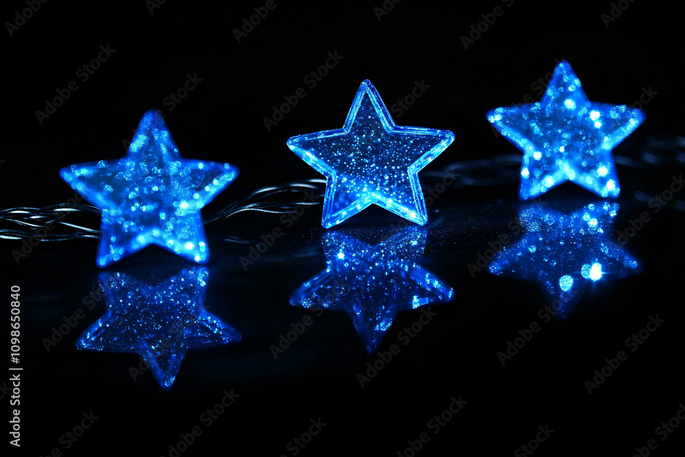 Obraz premium three illuminated blue stars with glittering textures reflected on a glossy black surface creating a festive ambiance 