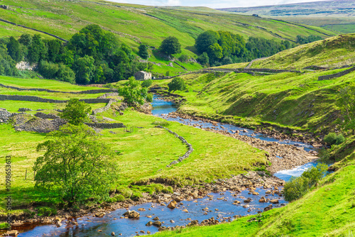 Swaledale in the Yorkshire Dales, UK and the River Swale running through the tiny hamlet of Keld with drystone walling, stone barns or cow houses and lush green meadows.  Space for copy.  Horizontal