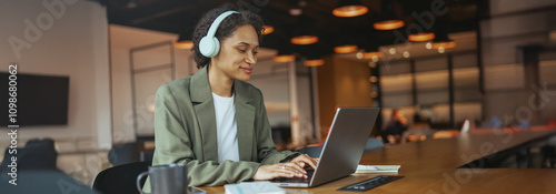 Woman iusing personal computer with headphones at table in nice modern coworking office photo