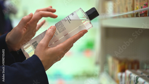 Close-up hands hold transparent bottle of body wash or shampoo. Customer reading label with ingredients, examining composition in cosmetics store, choosing cosmetic product, making purchasing decision photo