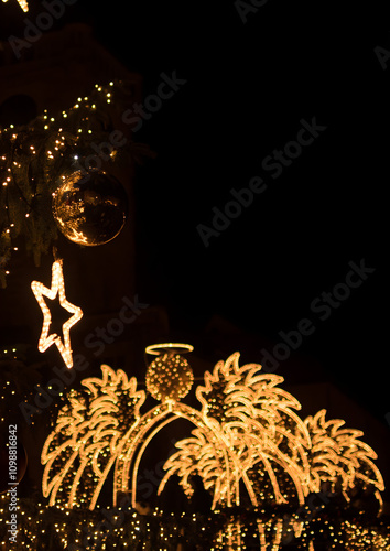 An image featuring an illuminated angel in the background, with a decorated branch of ornaments in the foreground for Christmas season