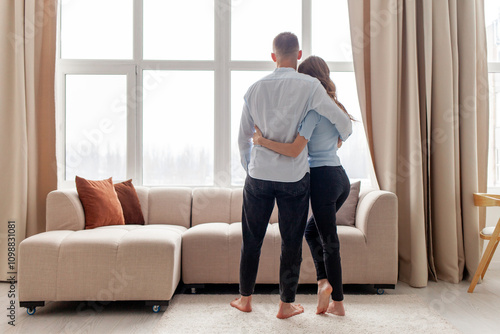 Fotografie young couple in love stands at home hugging and looking out the window near the