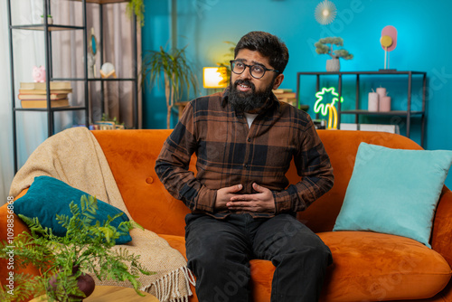 Bilde på lerret Indian young man sitting on sofa feeling sudden strong abdominal stomach ache, gastritis problem