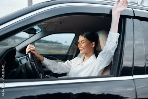 A woman sits in the driver's seat of a car with her hands raised, firmly gripping the steering wheel, expressing excitement or triumph