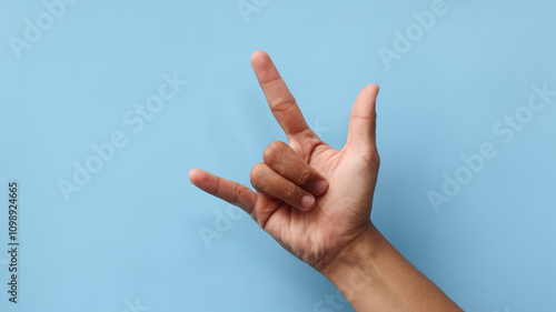 Rocker hand showing horns or rock gesture. Man's hand gesturing rock and roll, heavy metal, devil horns gesture or I love you on blue background