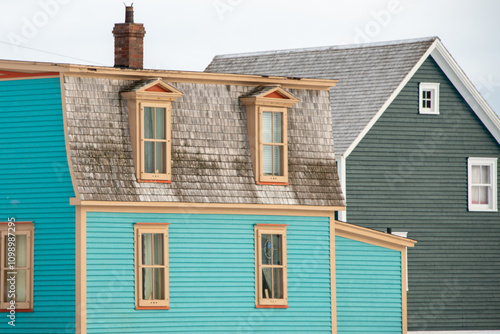 A large blue historic building with a mansard roof and two dormer windows. The house has a bright red wooden door and multiple glass double-hung windows. 