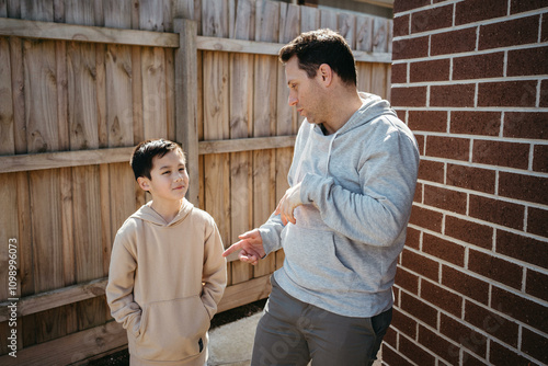 Middle-aged man making funny face with a boy whos hands are in his hoodie pocket. photo