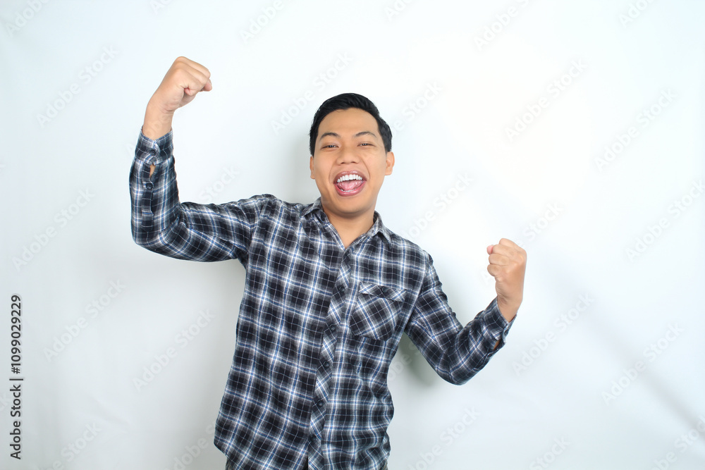 Fototapeta premium cheerful asian man raising fist showing winning and success gesture expression wearing casual shirt isolated on white