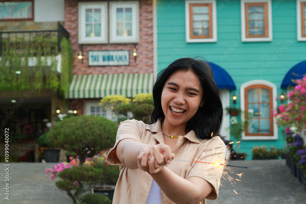 Fototapeta premium new year eve celebration concept. attractive asian young woman holding sparkler with laughing happy in outdoor garden of vintage house yard