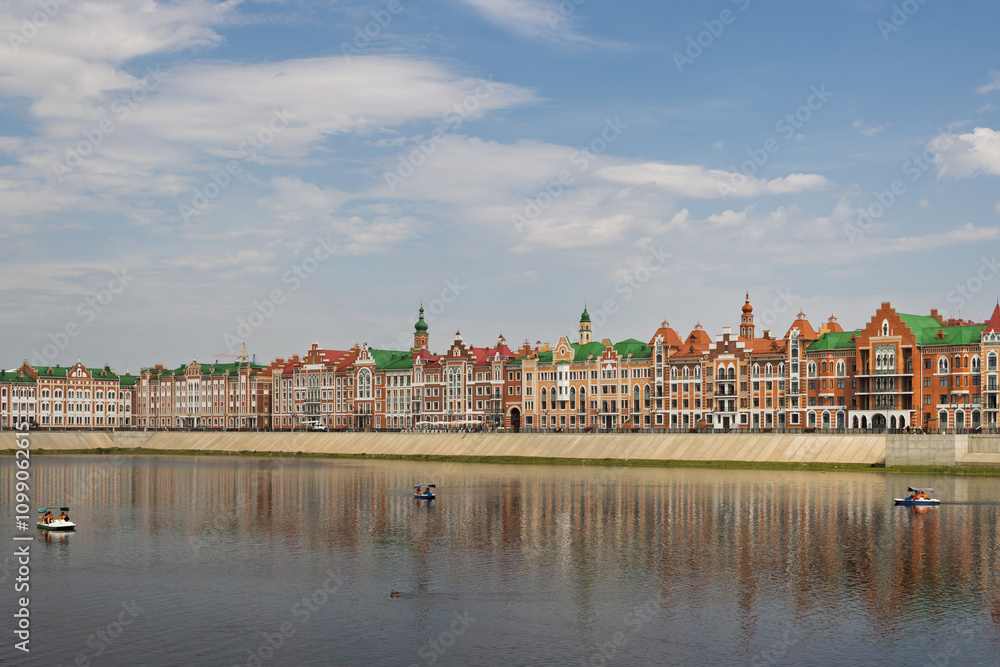 Obraz premium Yoshkar-Ola city, Mari El Republic, Russia. View of the Malaya Kokshaga River and the Brugge embankment in the center of Yoshkar-Ola. Beautiful colorful buildings on the river bank.