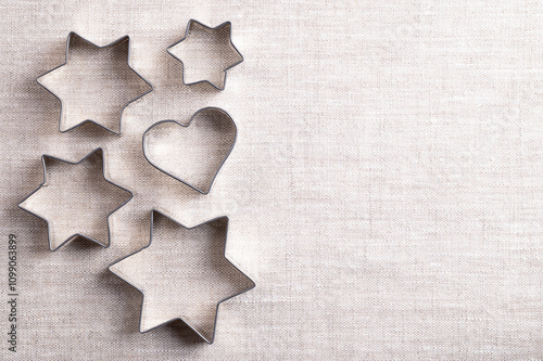 Cookie cutters on linen fabric, with empty space for text. Traditional biscuit cutters, tools to cut cookie and biscuit dough. Cutouts made of tin in star shapes of different sizes and a heart shape. photo