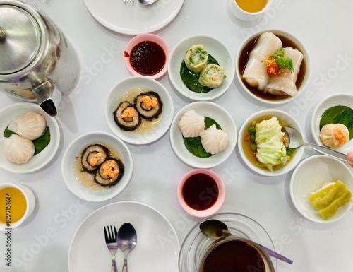 many kinds of Chinese style steamed dim sum in white dishes and hot Chinese tea and local hot black coffee on white table