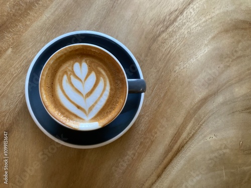 hot cappuccino coffee with gorgeous lily flower latte art in dark blue cup on natural wood table with beautiful wood grain with copy space on the right side of frame