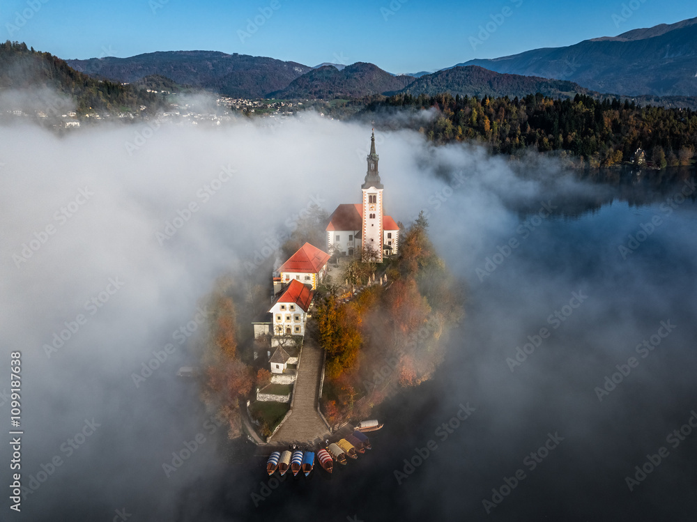 Bled, Slovenia - Aerial view of beautiful Lake Bled (Blejsko Jezero) with Pilgrimage Church of the Assumption of Maria on a small island with Pletna boats and fog over the lake on an autumn morning
