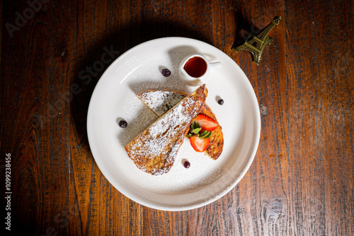 Top view of a plate of fench toast into triangular pieces with powdered sugar and garnished with a fresh strawberry and a sprig of mint photo