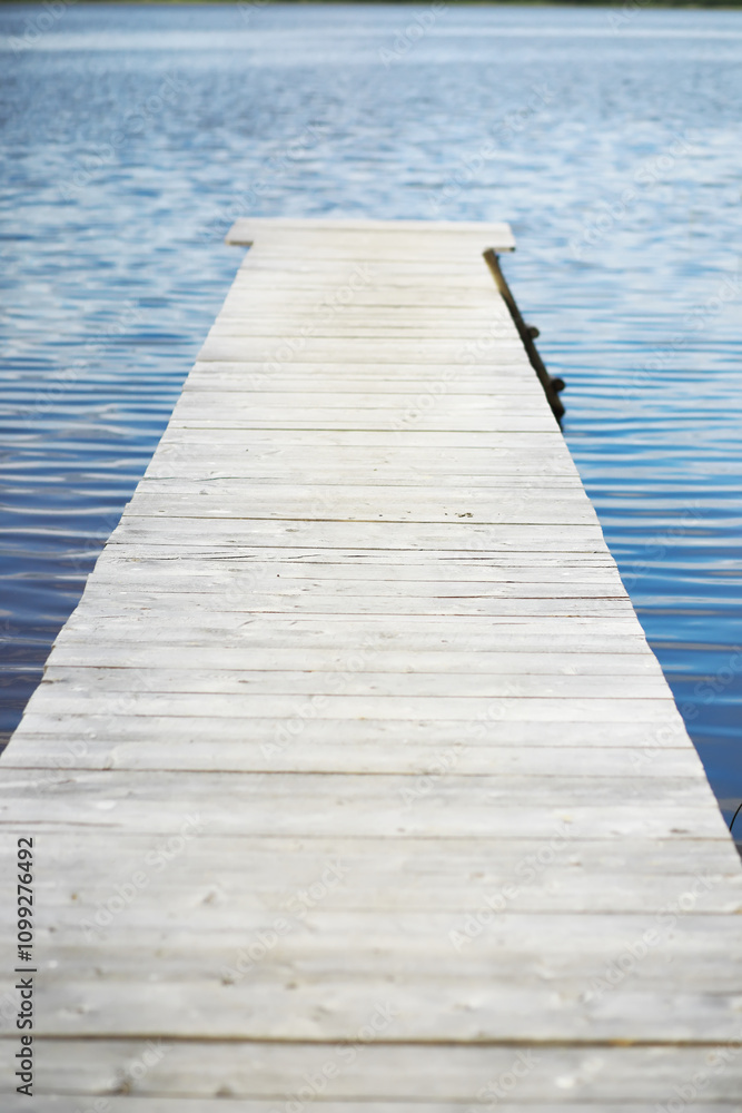 Fototapeta premium Wooden Pier Extending into Calm Lake Waters with Clear Blue Sky Reflections