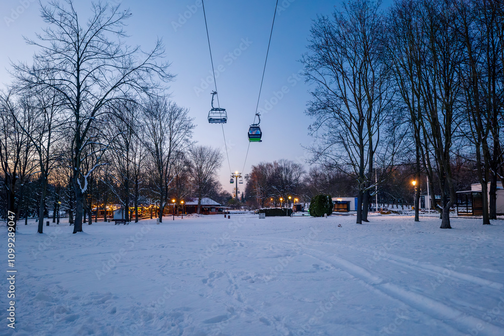 Beautiful winter in the park. Illuminated restaurants in the background. The longest lowland cableway in Europe