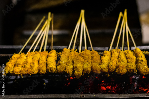 Close up of Sate kelapa or sate klopo or coconut satay, chicken or meat satay with coconut ingredient on red fire grilling by people. Traditional satay from Surabaya, East Java, Indonesia. photo