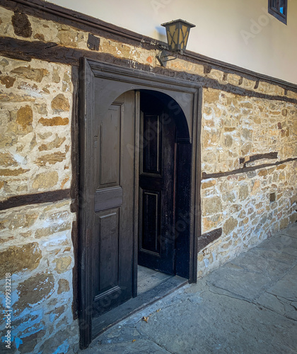 A pair of dark wooden doors stand open against a backdrop of stone walls and a charming lantern.