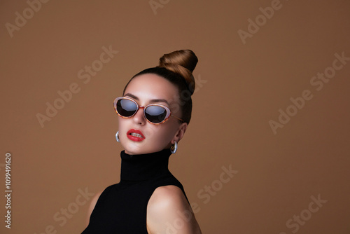 Fashion beauty portrait of a beautiful young woman with a hair bun is wearing a cat eyes sunglasses and silver earrings photo