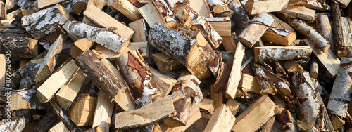 Stack of birch firewood with hand chopping block. Chopped firewood for winter. Lot of firewood - harvesting wood for heating the house. Banner format. Chopped firewood background and texture.