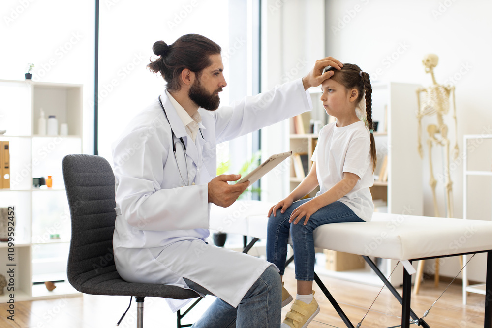 Obraz premium Caucasian male doctor checks health of little sick girl with high temperature sitting on medical couch. Professional medical setting includes necessary equipment for thorough health assessment