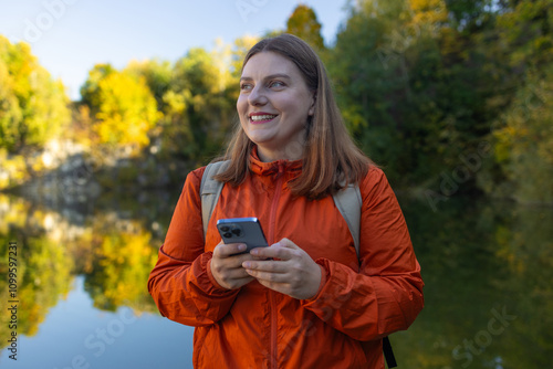 Traveler hiker 30s woman holding smartphone in a hand and using GPS app with trekking in autumn mountains outdoor. 