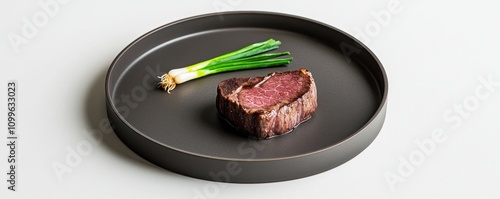 A beautifully plated steak with green onions on a sleek black plate, showcasing modern culinary presentation.