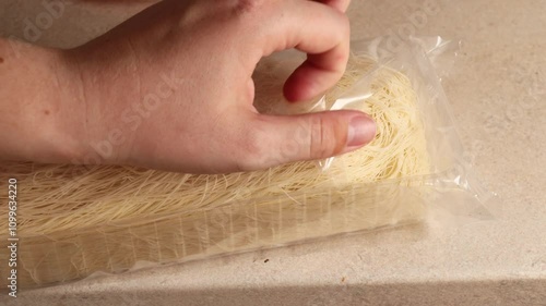 Opening packaging of kataifi dough. Close-up of hands unwrapping delicate kataifi pastry, ready for traditional Middle Eastern and Mediterranean desserts.  photo