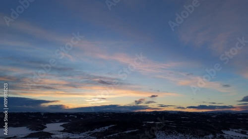 Stunning aerial drone footage of a snow-covered village nestled in a serene valley, surrounded by majestic mountains. Capture the enchanting winter landscape with breathtaking sunset hues. photo