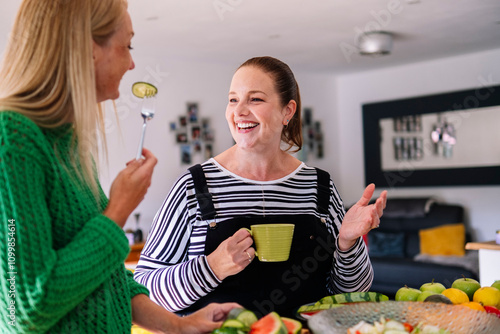 Happy woman holding coffee cup with friend eating cucumber at home photo