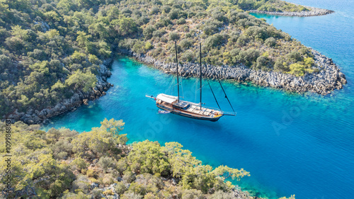 A gulet ship anchored in crystal-clear waters, surrounded by lush green hills and a serene coastal landscape. photo