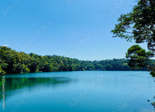 A tranquil view of Lake Eacham in Queensland, Australia, with its calm blue waters surrounded by lush forest