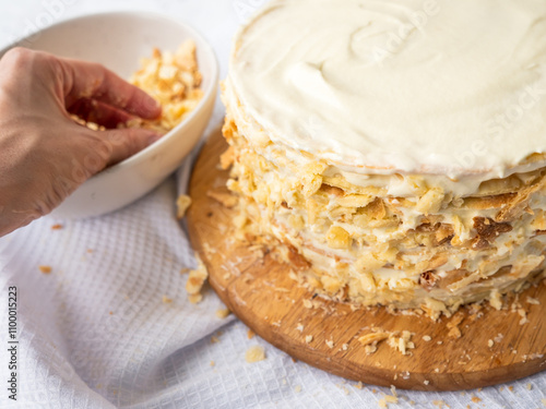 Obraz na płótnie Hand sprinkling decorating crumbs over a pile of thin round layers spread with vanilla custard, bowl of dough crumbs on a white waffle towel in the blurry background. Shortcrust puff pastry Napoleon w salonie