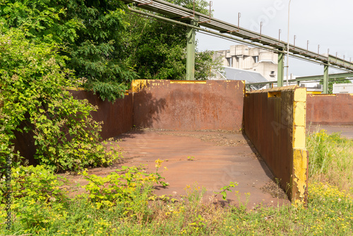 Wallpaper Mural Old rusty huge open skip standing on the ground and is partially  overgrown. Concrete factory complex with pipes the background. Torontodigital.ca